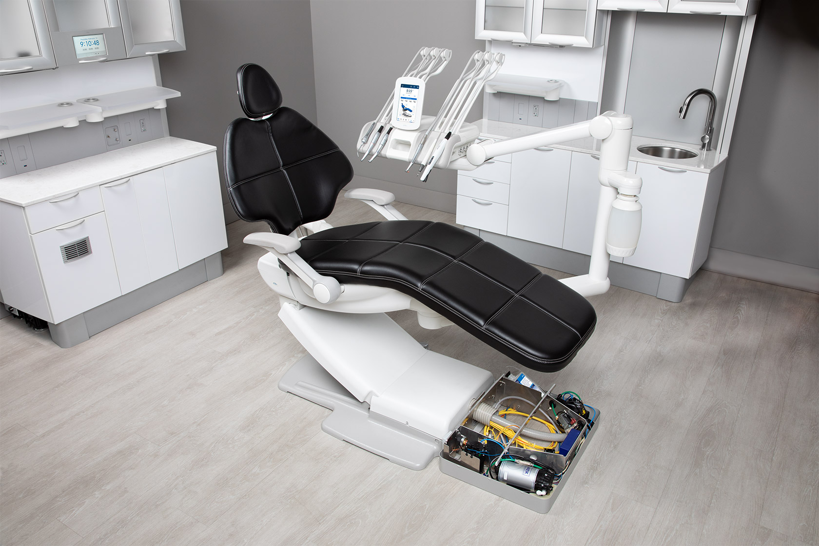 Dental chair with black upholstery, delivery system, and open A-dec Maintain floor box in a dental operatory