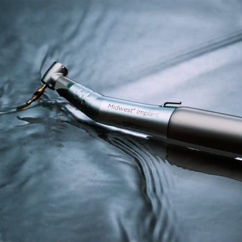A Dentsply Sirona Midwest Implant dental handpiece and dental motor lie in shallow water